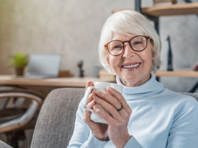Eldre kvinner holder i kaffekopp. Smiler. Foto